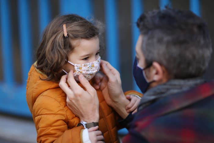 Adult adjusting a face mask on a young child wearing a coat