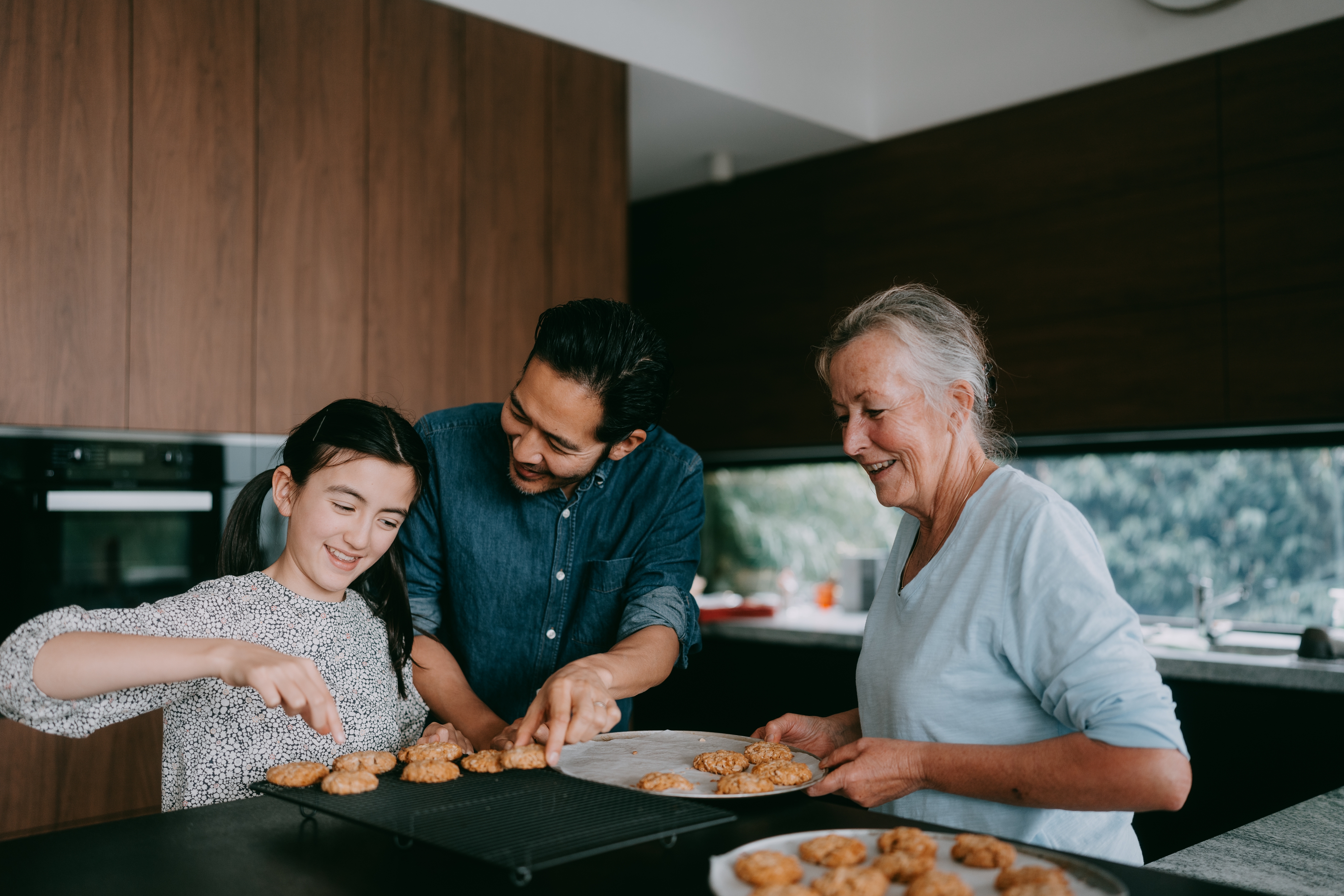 En familie med tre gledelig forbereder informasjonskapsler på et moderne kjøkken, med en ung jente, en mann og en eldre kvinne