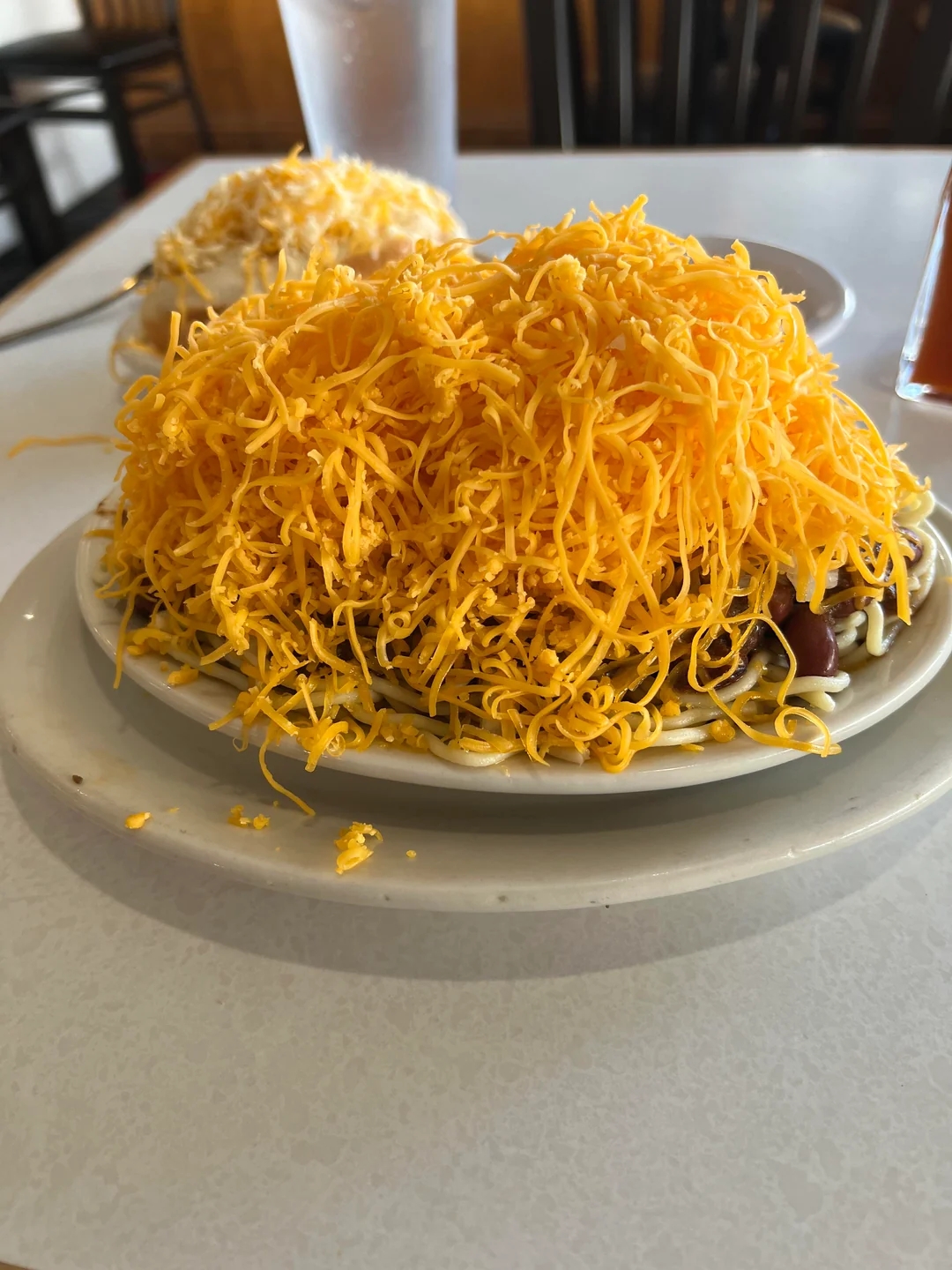 Plate of spaghetti topped with shredded cheese, with another similar dish in the background