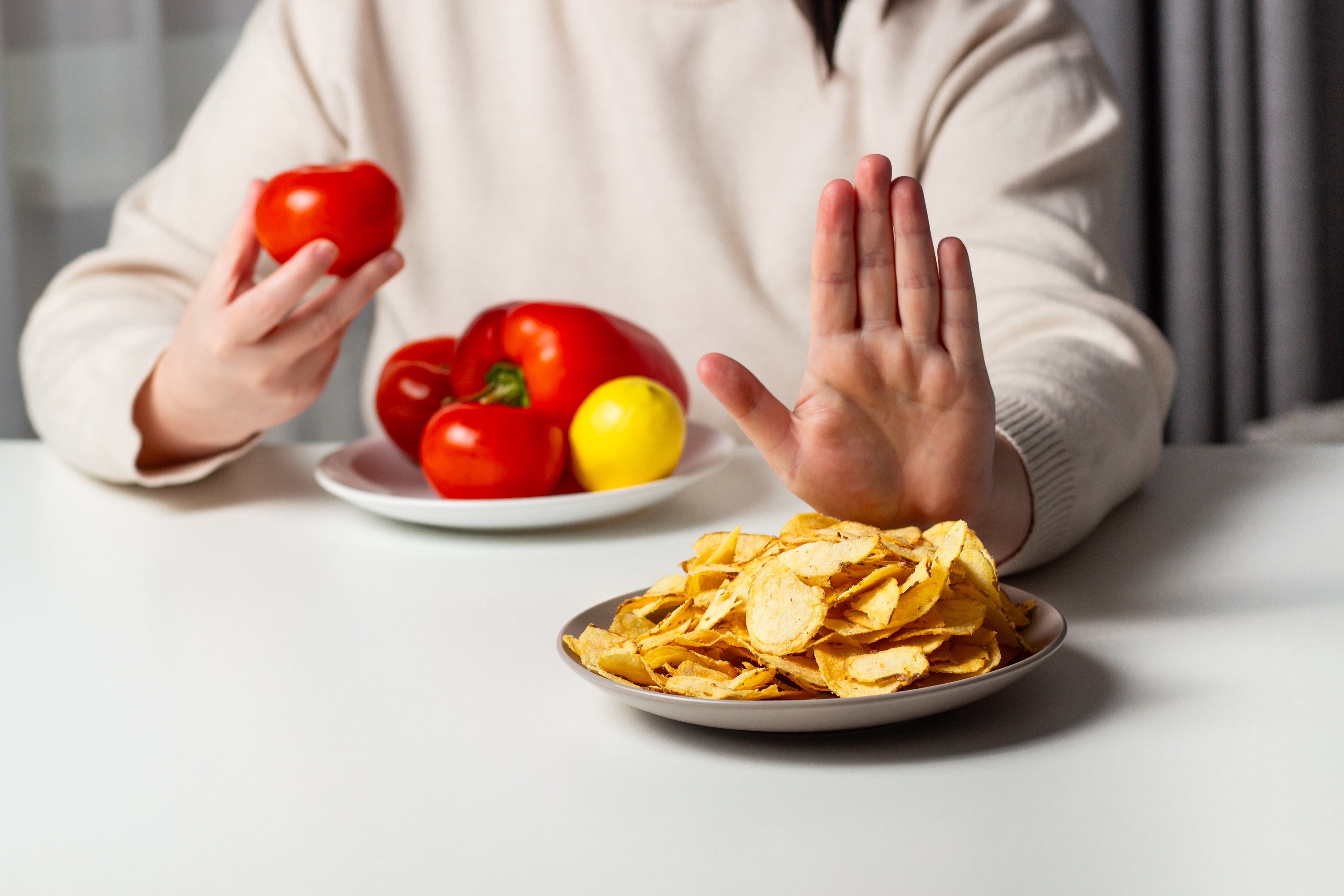 Personen skyver bort plate med flis og holder en tomat, med flere grønnsaker på en tallerken i bakgrunnen