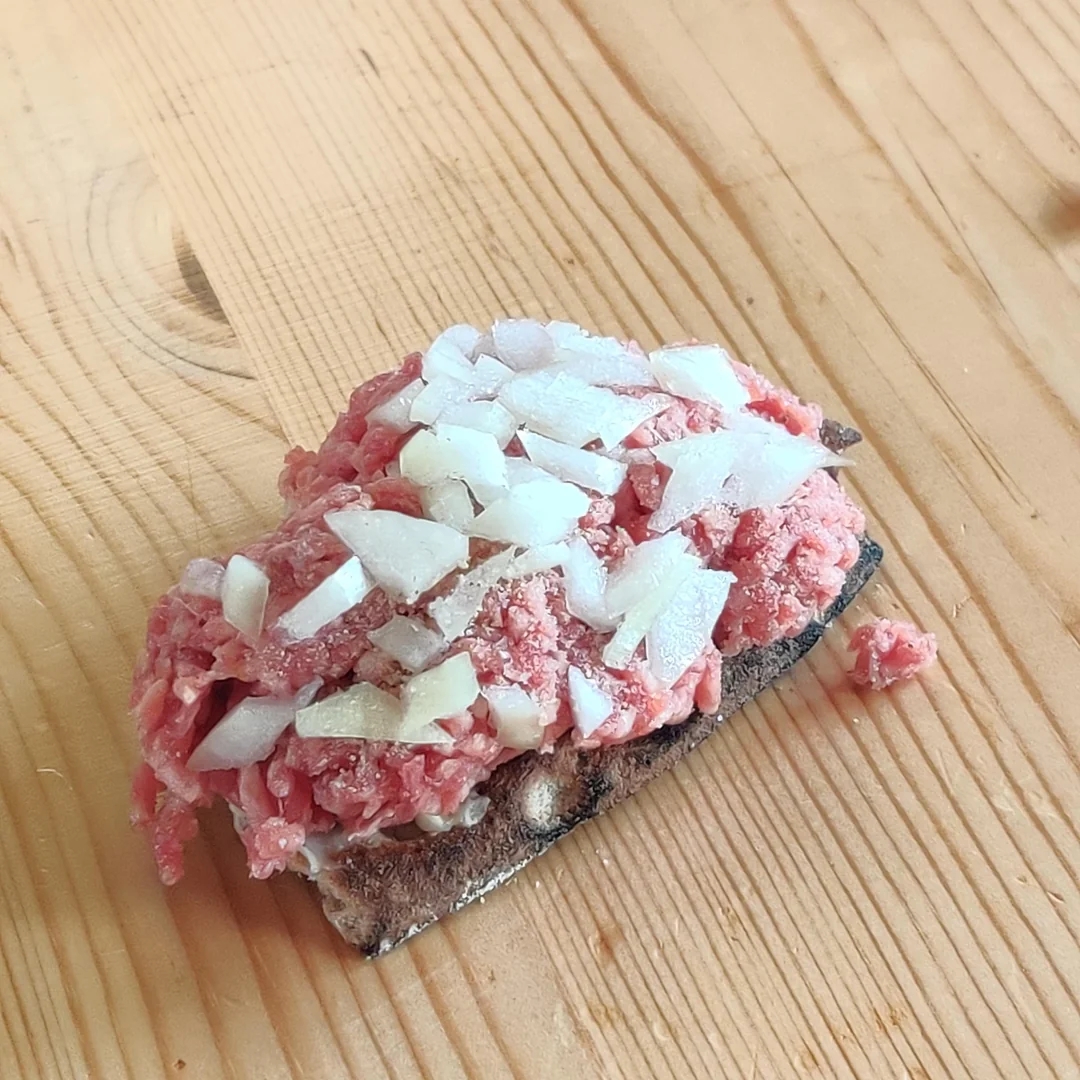 Minced raw meat topped with diced onions on a slice of bread on a wooden surface