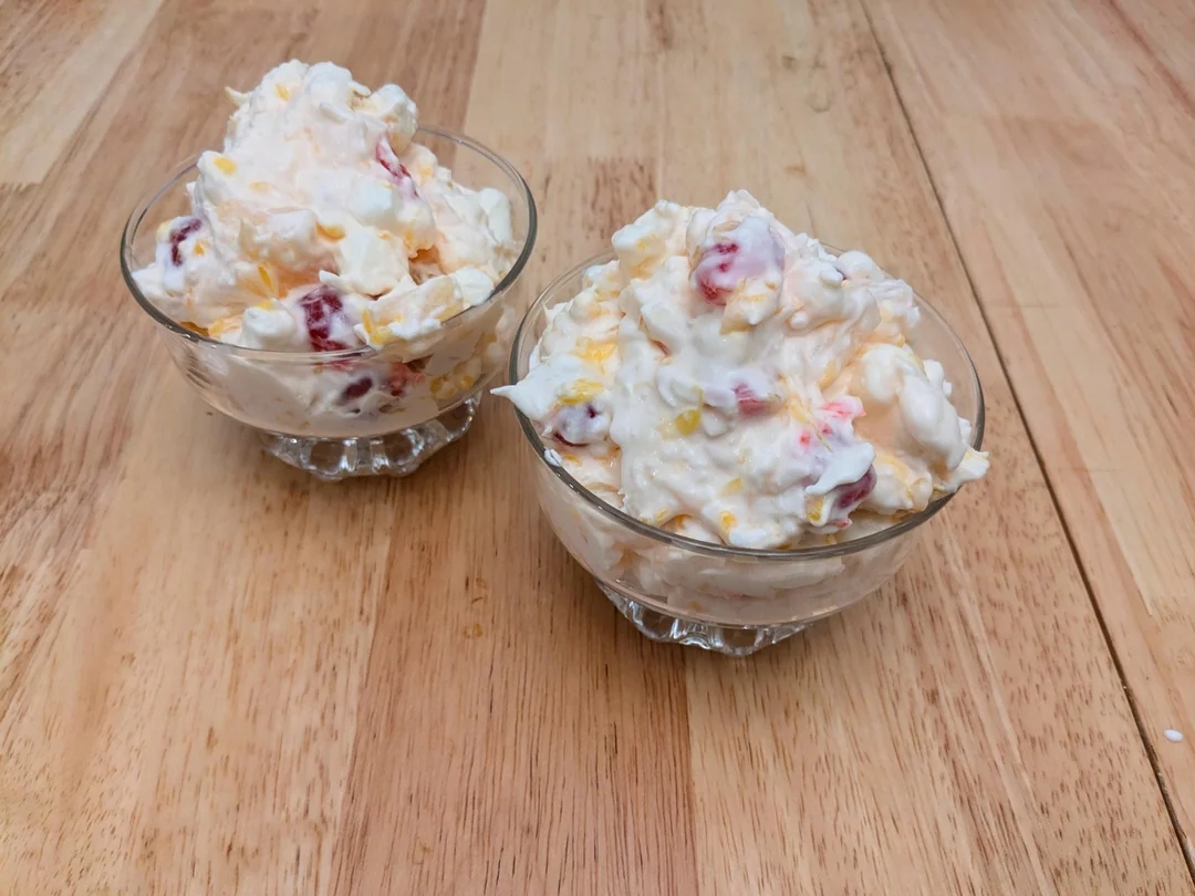Two glass bowls filled with a creamy fruit salad, including pieces of fruit visible on a wooden table