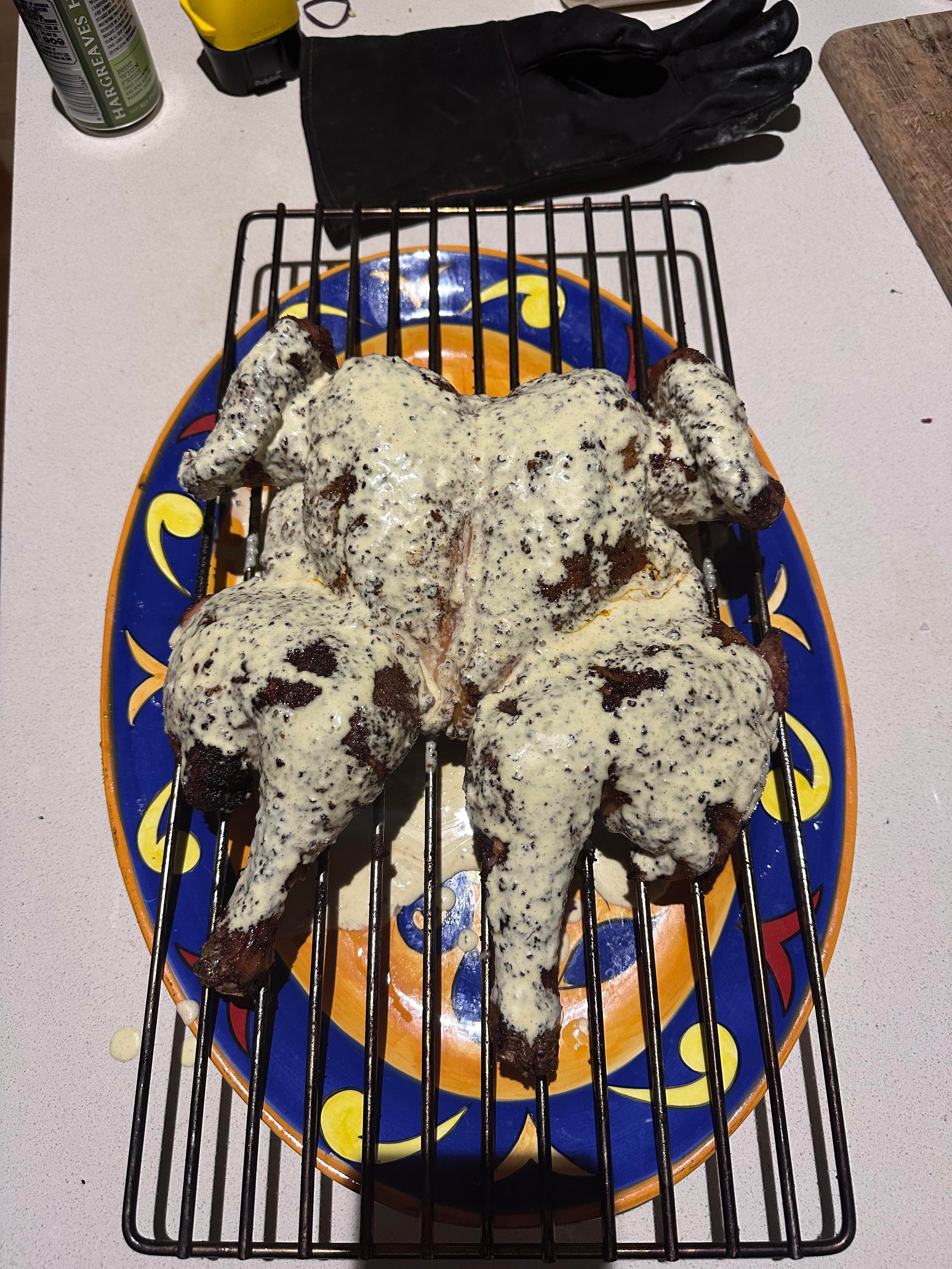 Grilled spatchcock chicken on a vibrant patterned plate, coated in creamy sauce, placed on a cooling rack
