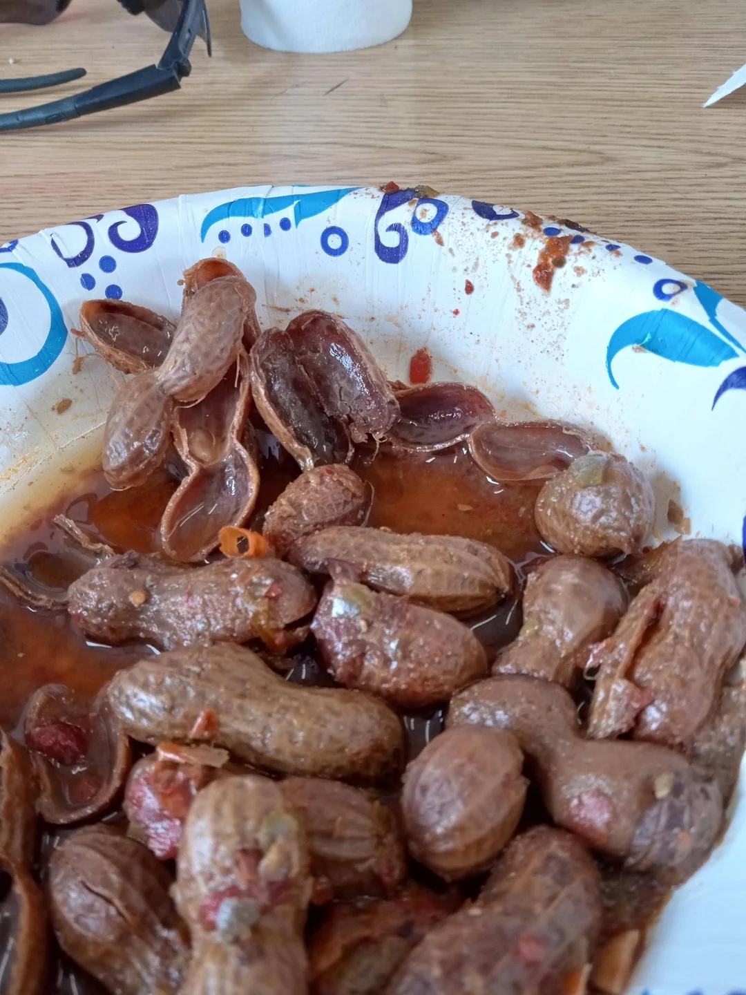 Boiled peanuts in a paper bowl on a wooden table, with a pair of sunglasses nearby
