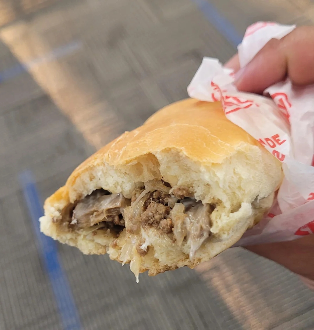 Person holding bitten sandwich with visible meat filling inside a bun