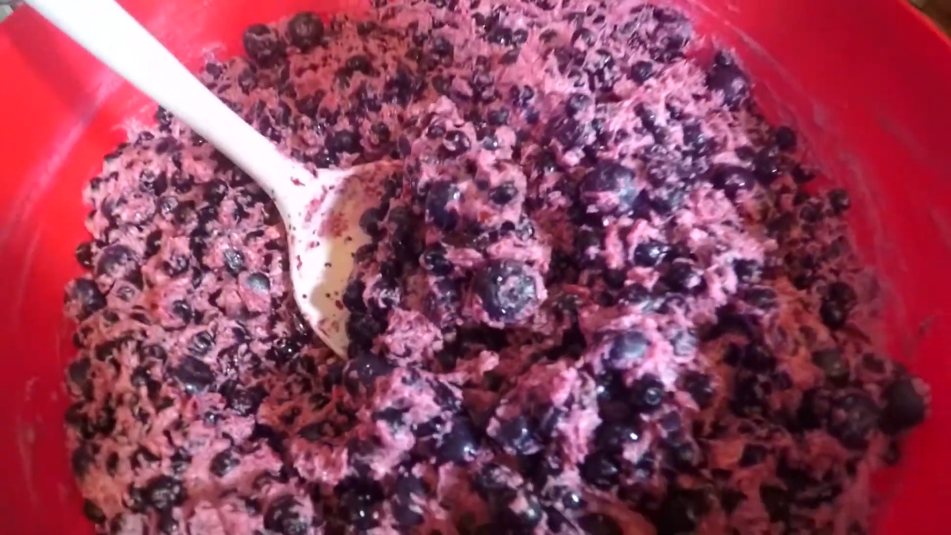 Mixing bowl with a spoon stirring ingredients, including blueberries, suggesting preparation of a blueberry-based dish
