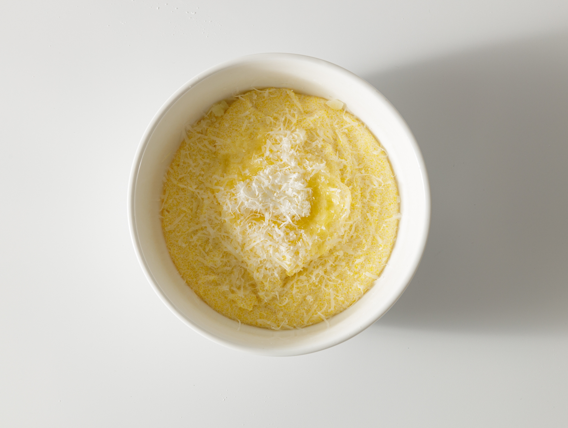 Bowl of creamy polenta topped with grated cheese, viewed from above