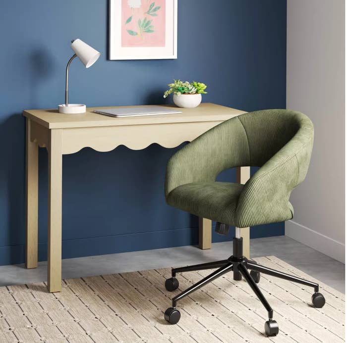 Modern location bureau with beige desk, task lamp, and greenish swivel seat connected wheels. Neutral decor promotes a minimalist buying aesthetic