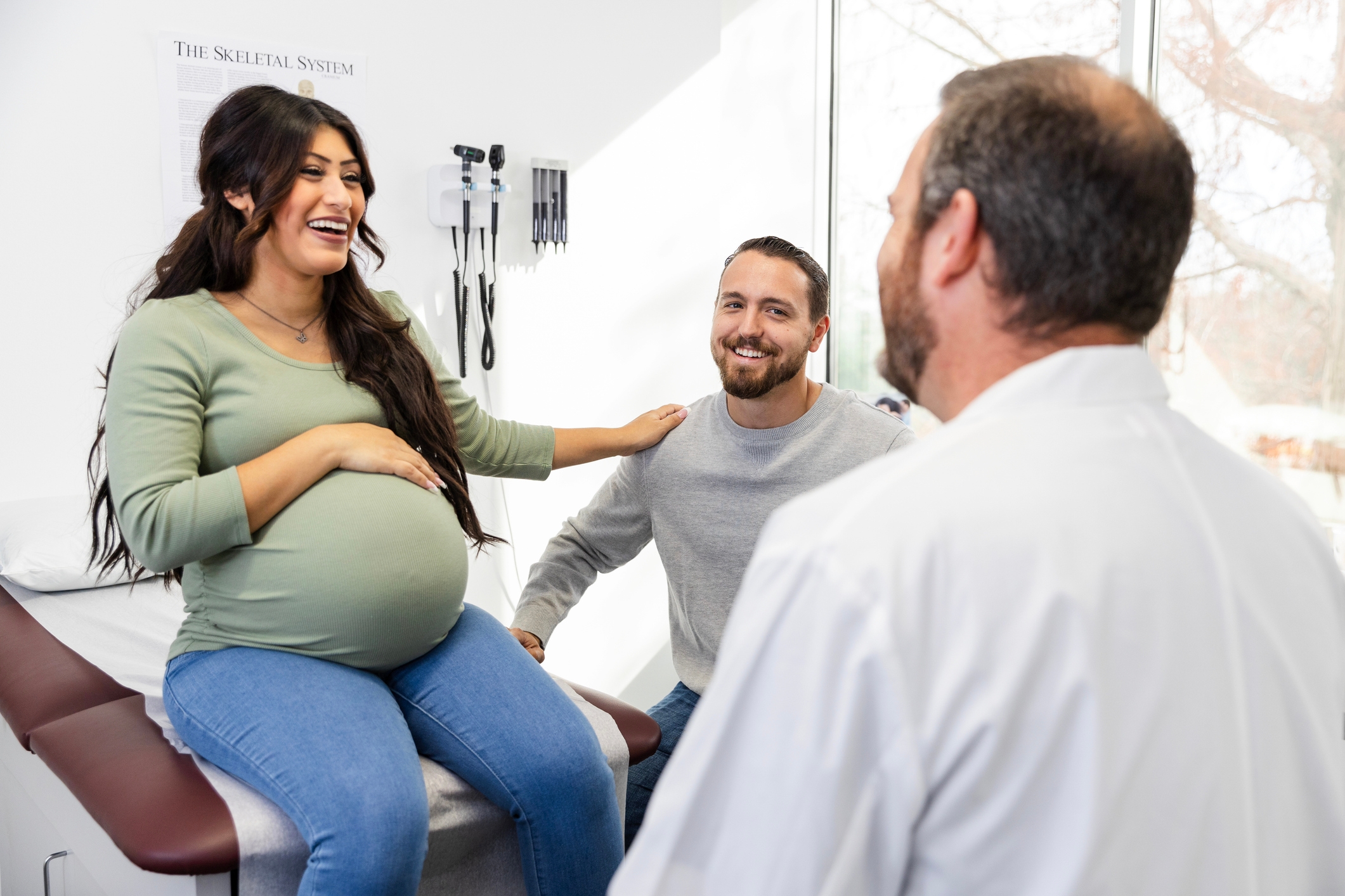 Pregnant woman smiling with partner and doctor in an exam room, discussing a prenatal check-up