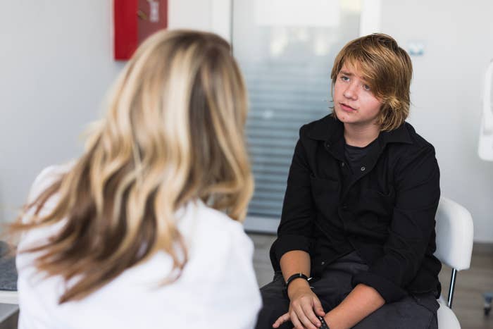 Teen in black shirt sitting in a chair, listening attentively to someone nearby during a conversation in an indoor setting