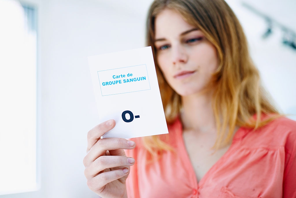 A person holds a card labeled &quot;GROUPE SANGUIN O-,&quot; indicating blood type. The focus is on the card, suggesting importance or relevance