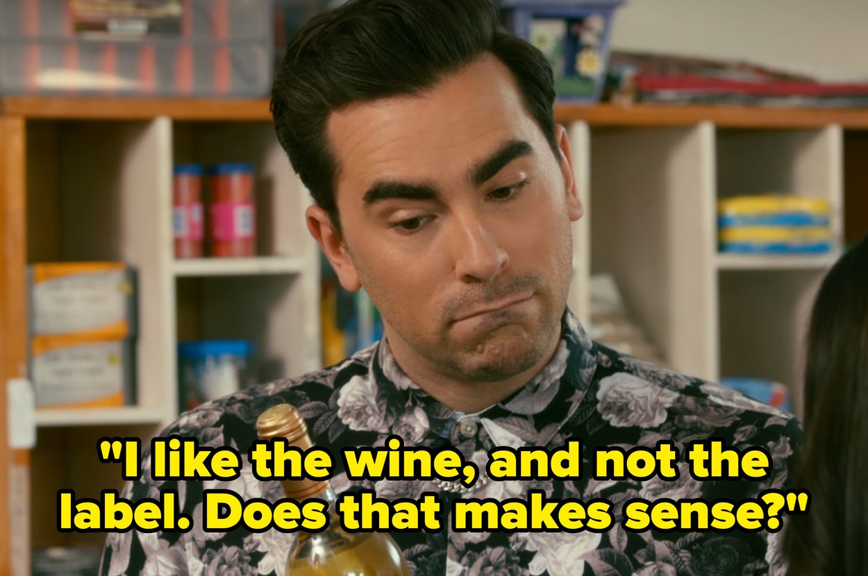 A person in a floral shirt holds a wine bottle, engaging in a conversation in a store setting