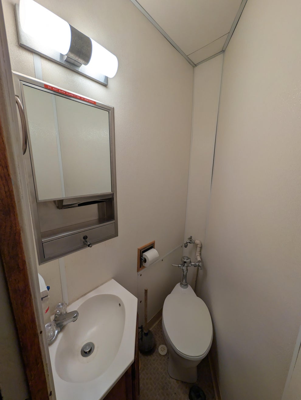 Small bathroom with a toilet, sink, mirror, and wall-mounted light fixture. Minimal decor and fixtures