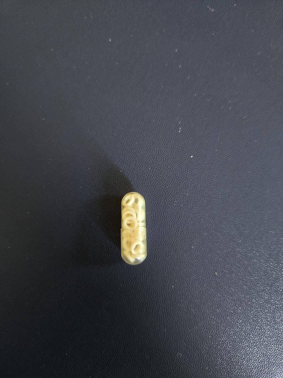 A transparent capsule containing small beads, placed on a plain surface
