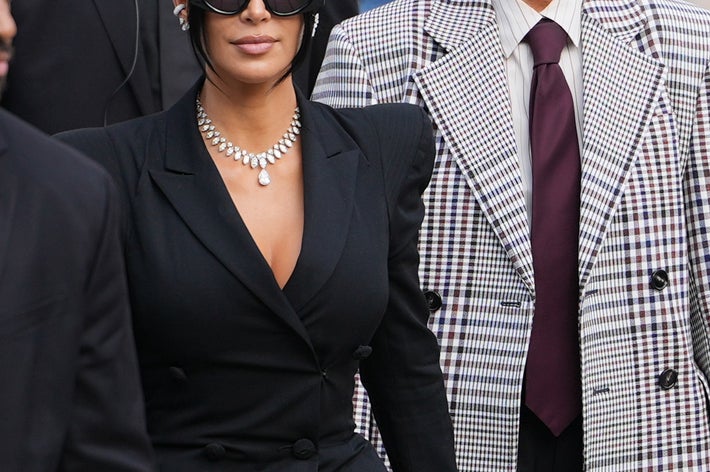 Two individuals in stylish black and white outfits, with sunglasses, walk past security personnel on steps outdoors