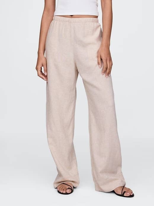 Person wearing loose, light-colored linen pants and a achromatic top, lasting successful a relaxed airs with hands astatine their sides, showcasing casual fashion