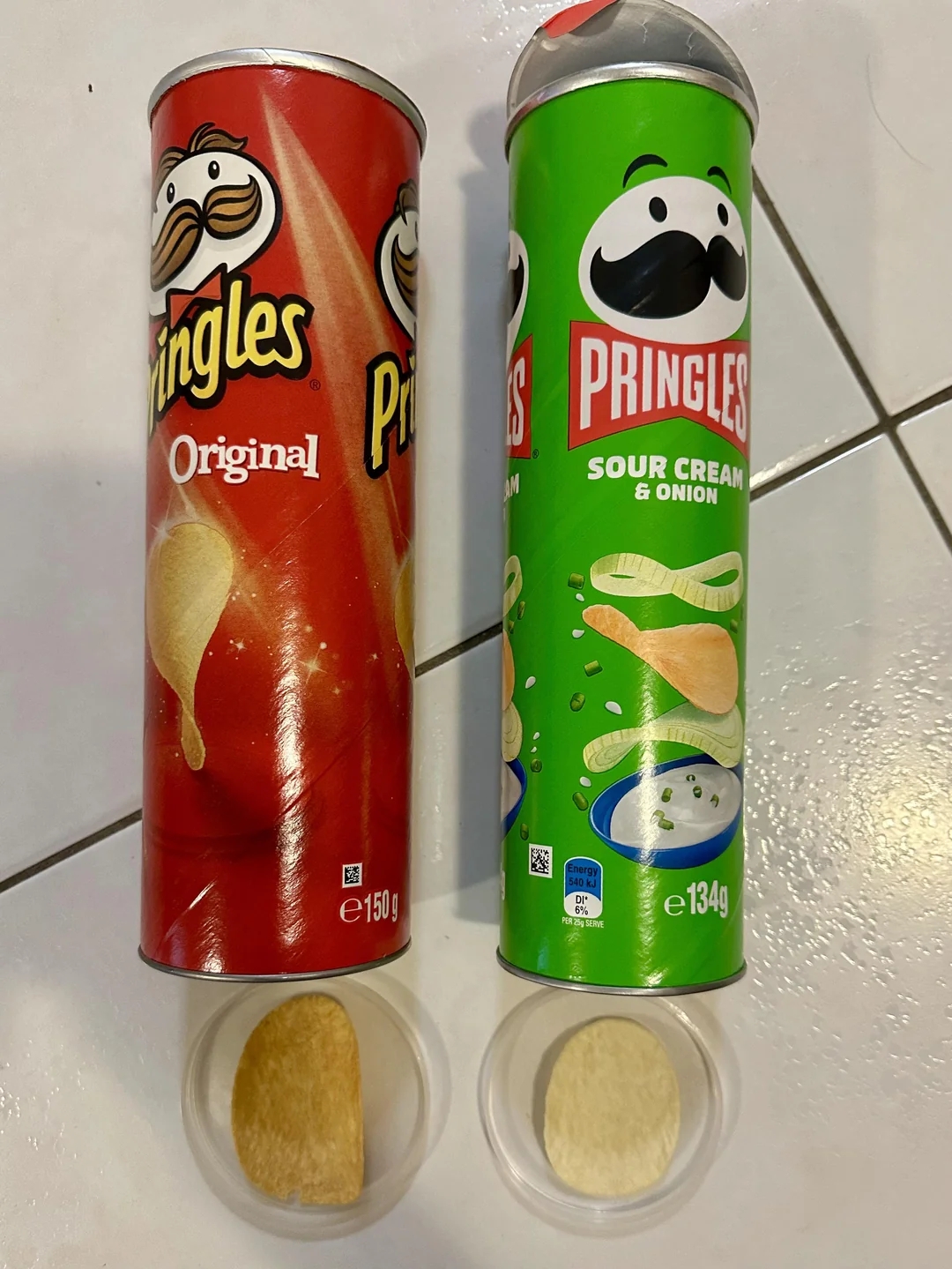 Two Pringles cans, Original 150g and Sour Cream &amp;amp; Onion 134g, placed side by side. Each can is slightly opened with a chip visible