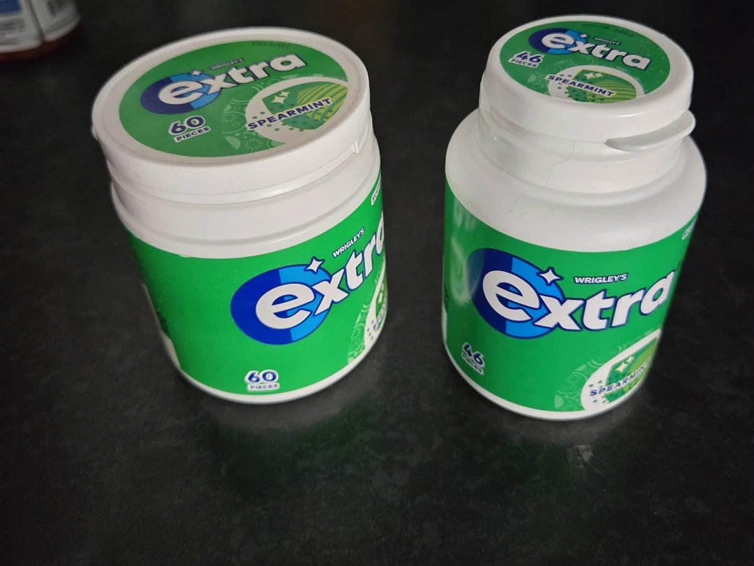 Two green containers of Wrigley&#x27;s Extra peppermint gum with 60 pieces on a dark surface, labels partially visible