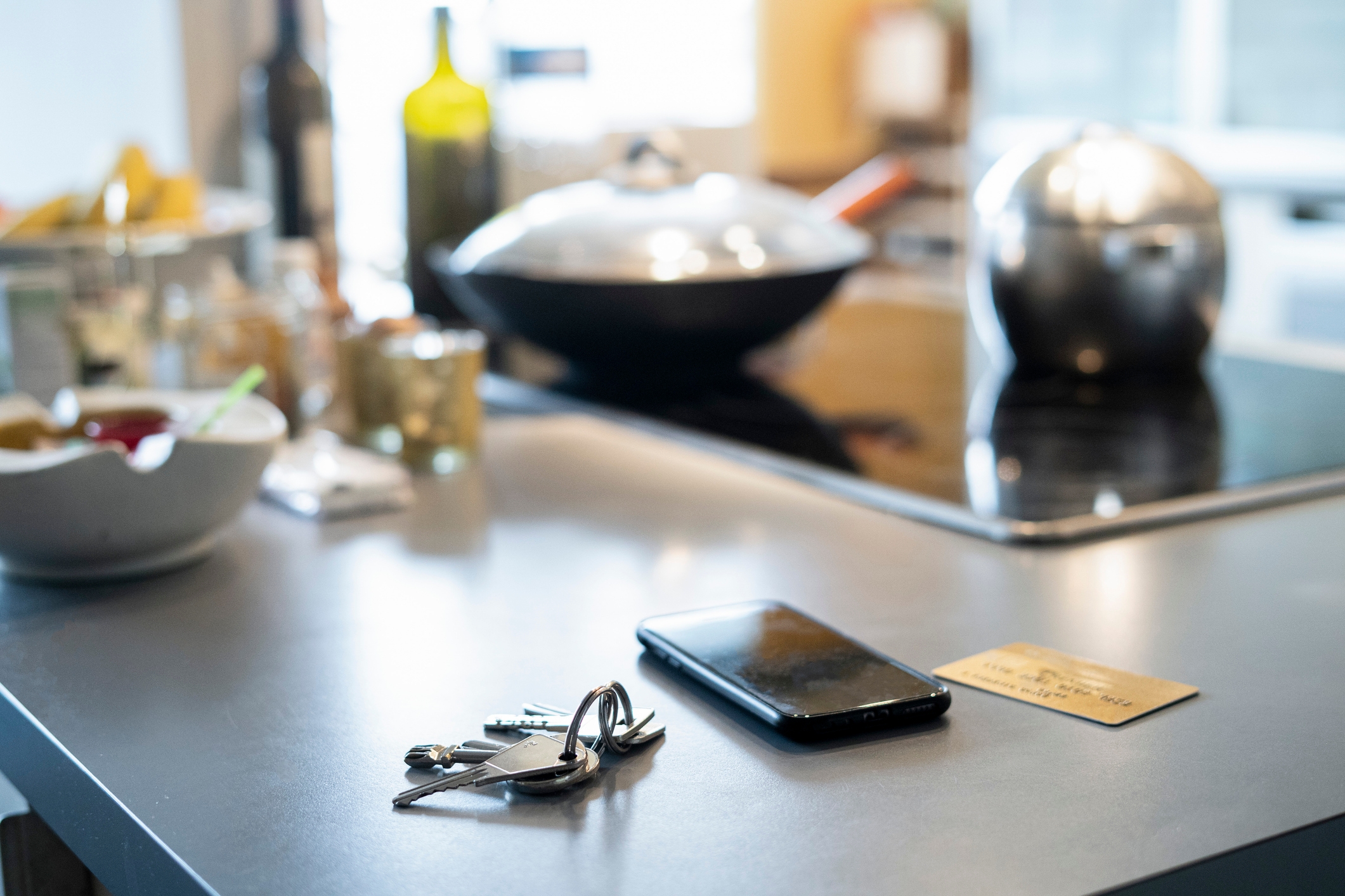 En kjøkkendisk med nøkler, en smarttelefon og et kort i forgrunnen; Kitchenware er uskarpt i bakgrunnen