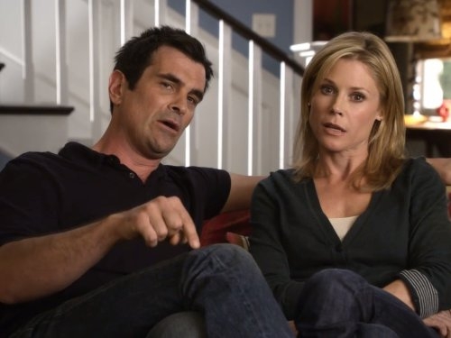 Two people sitting on a couch, engaged in conversation, with a staircase in the background