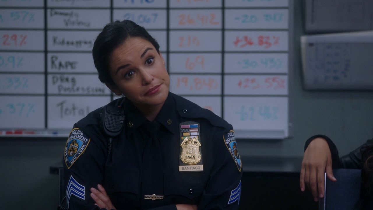 Police officer in uniform stands in front of a board with percentages, looking confidently into the camera