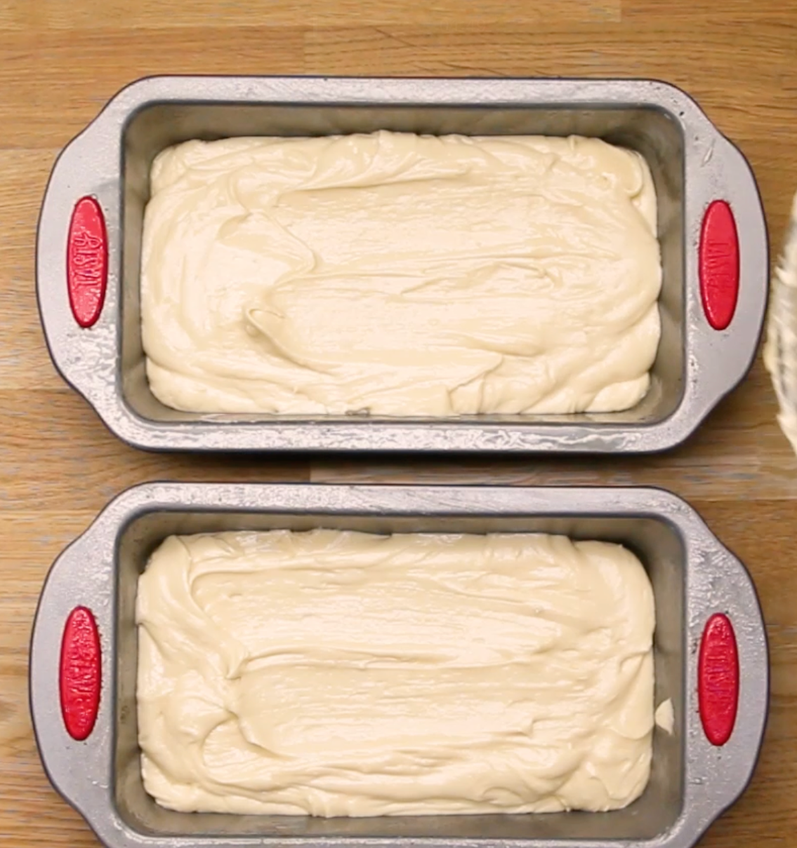 Two loaf pans filled with smooth cake batter rest on a wooden surface, ready for baking