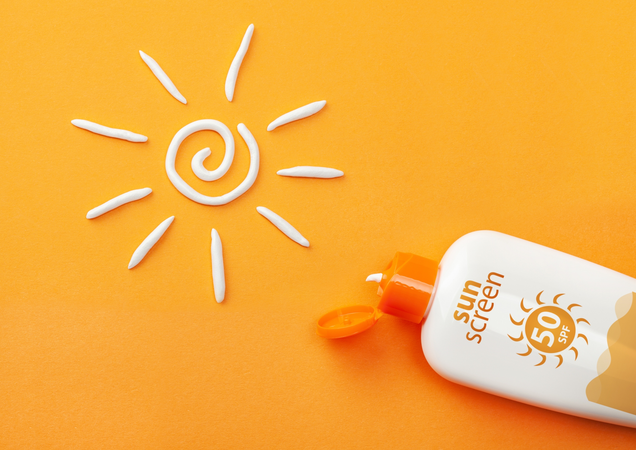 Solkremflaske på en oransje bakgrunn med SPF 50 -etikett, og en solform laget av solkremkrem ved siden av