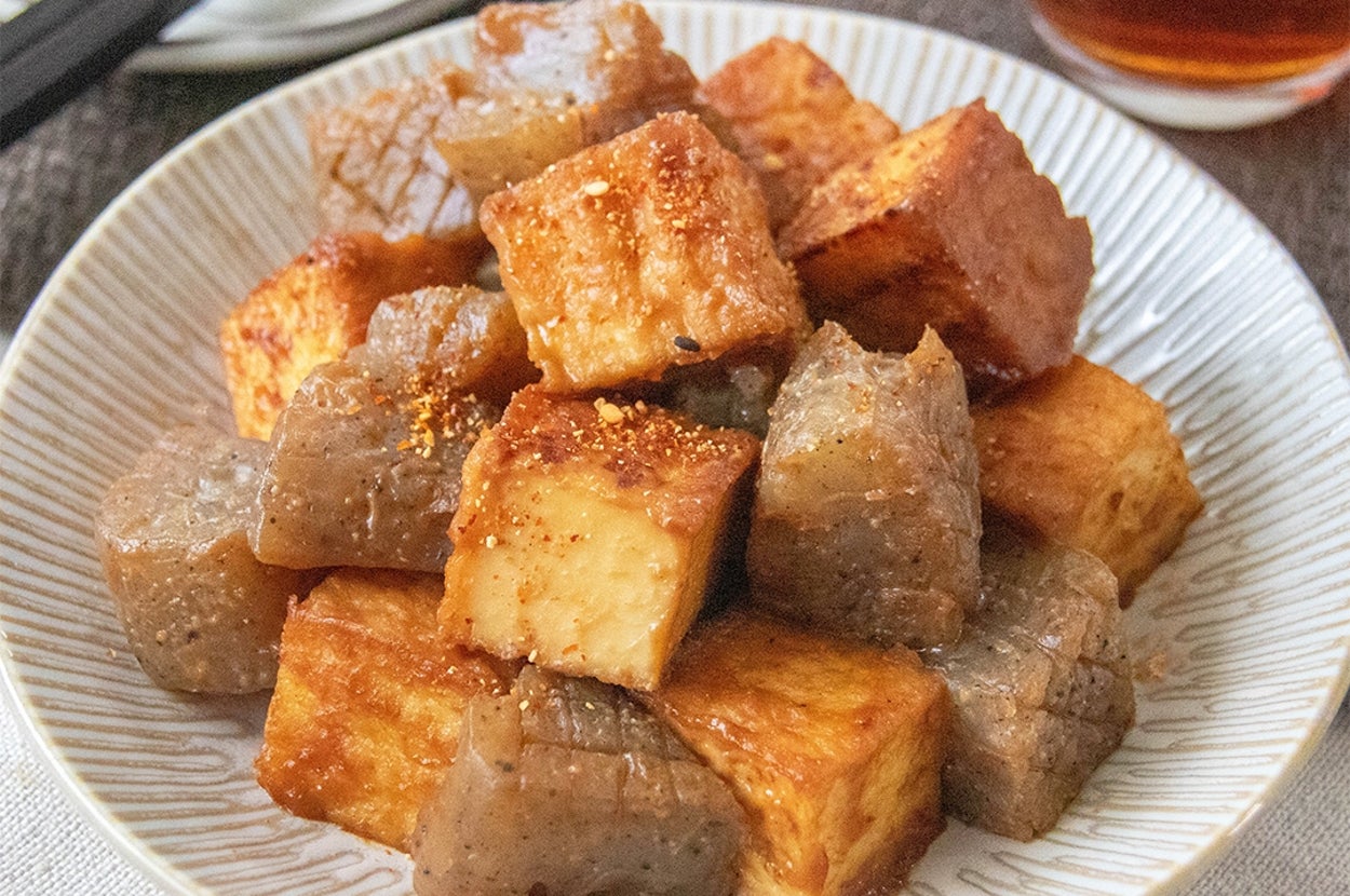こんにゃくと厚揚げのみそだれ炒めが白い皿に盛られている。背景にグラスと箸が見える。