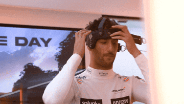 Person in a racing suit adjusts a virtual reality headset in a futuristic setting