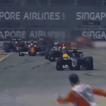 Race cars speed down a track, a person runs across ahead of them, creating a tense moment. The scene is from a high-speed motorsport event