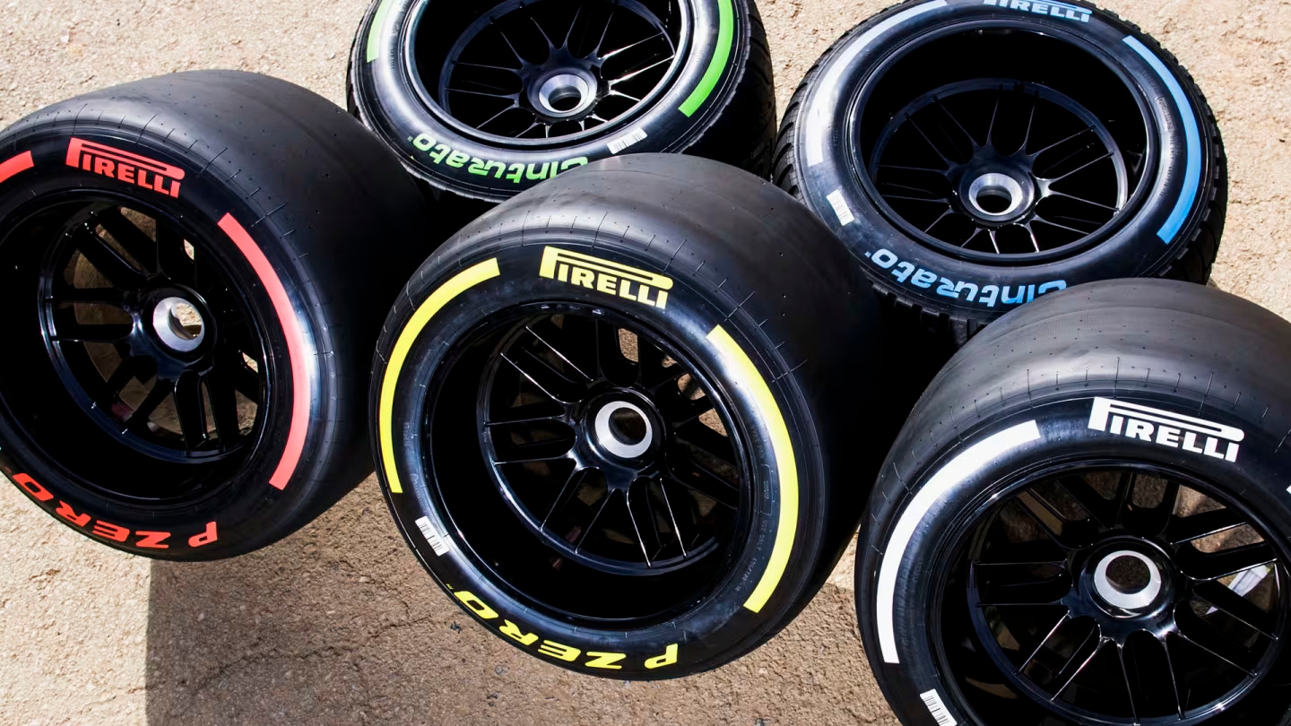 Five Pirelli racing tires with different tread markings displayed on a surface, showcasing variations in tire types and specifications