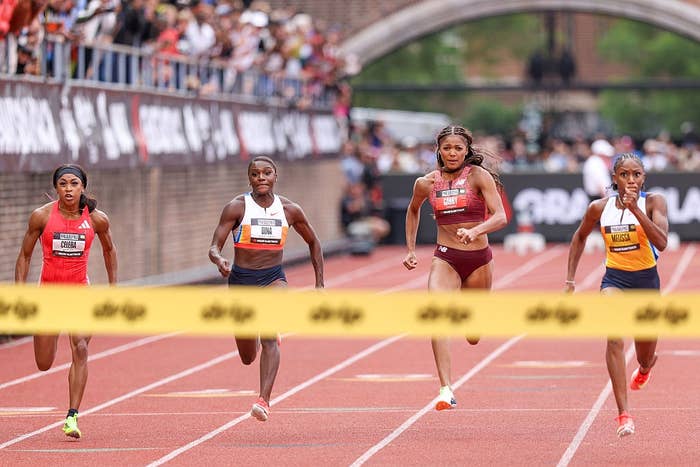 Four athletes running towards the finish line on a track during a race, with two athletes appearing to be in the lead