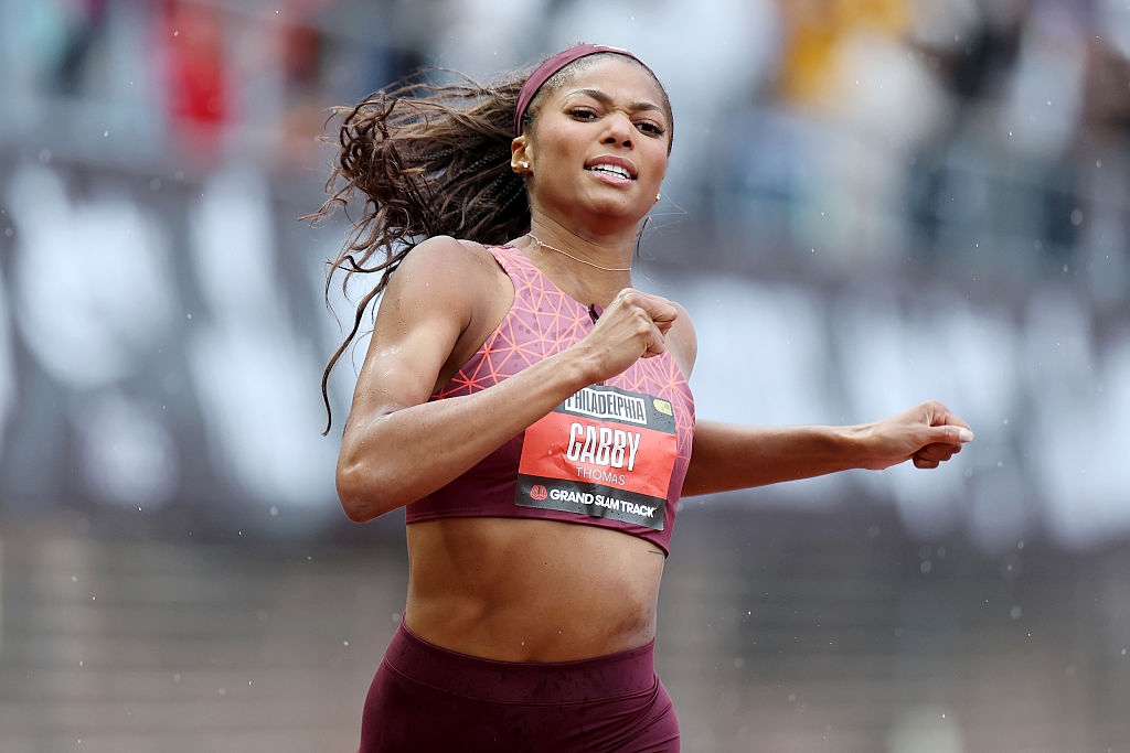 Athlete running in a track event, wearing sportswear with a patterned top and headband, showing determination and focus