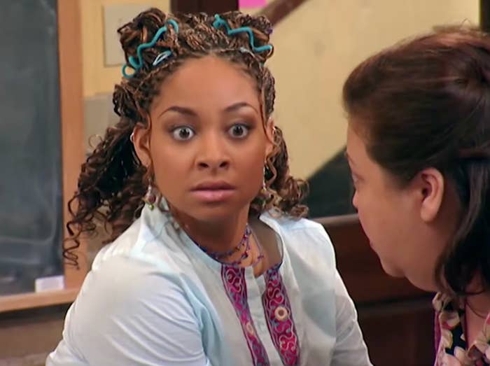 Two people in a tense scene. The one facing the viewer has wide eyes and braided hair, suggesting surprise or shock. The setting is indoors