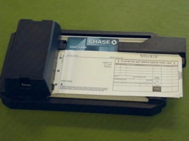 A vintage credit card imprinter with a Chase debit card and a receipt form placed in it on a green surface