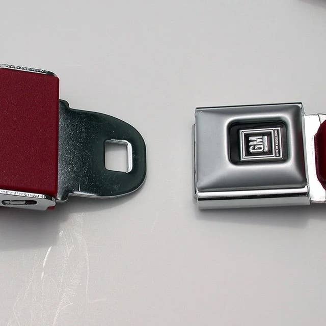 Close-up of a vintage GM car seat belt buckle with a metallic finish, highlighting retro automotive design