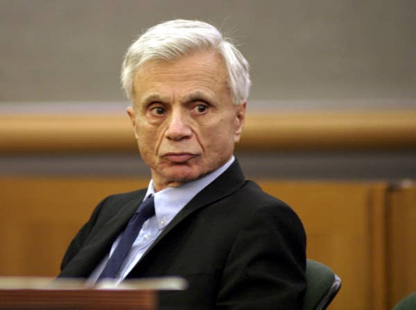 Older man in a courtroom, wearing a suit and tie, looking to the side