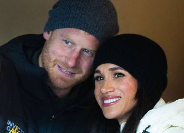 A couple smiling, both wearing beanies. The man has a beard, and the woman wears a white jacket. They appear happy and relaxed