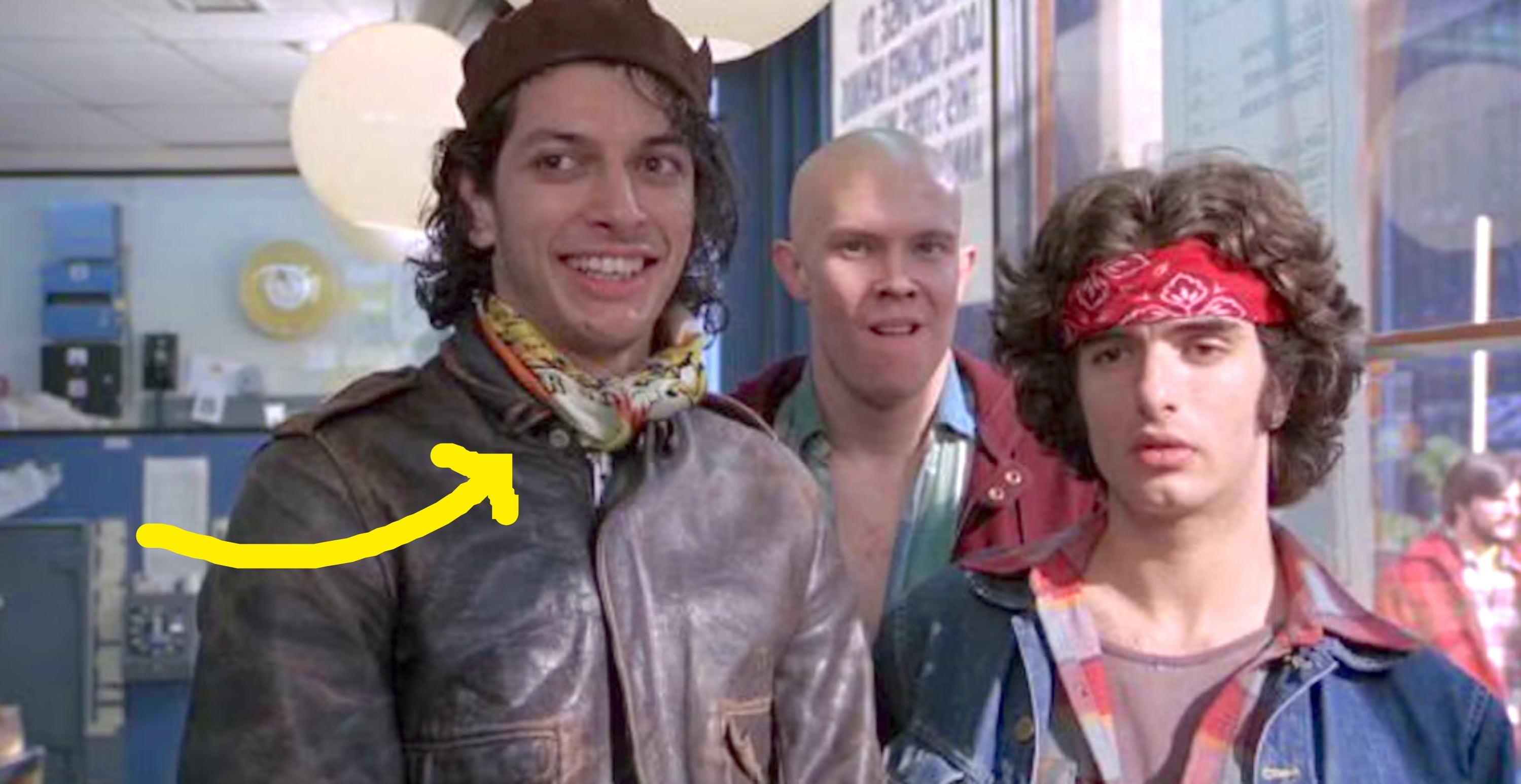 Three people in 80s-style clothing, including a leather jacket and bandana, standing indoors with a casual, amused expression