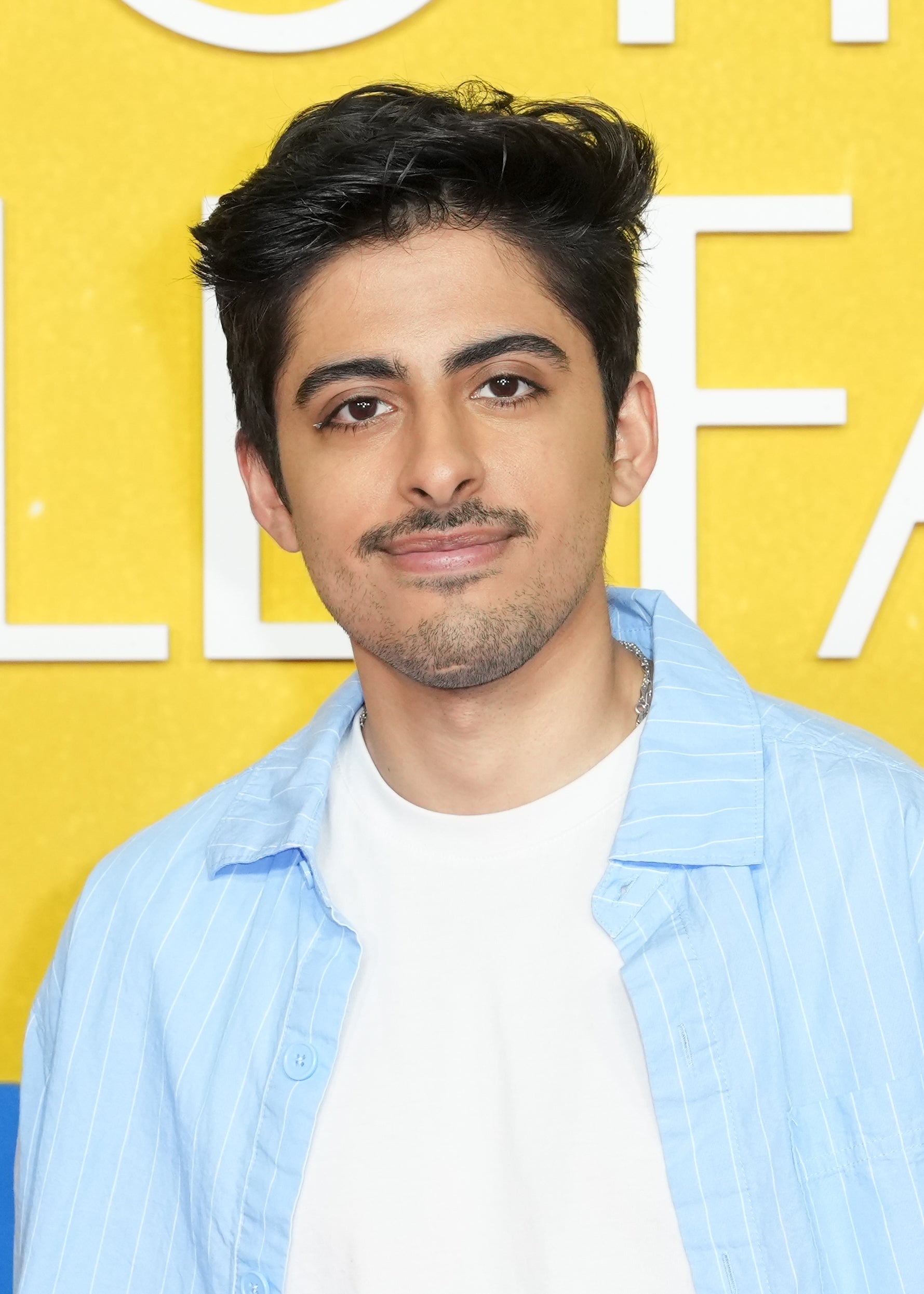Person with short dark hair wearing a white top and light blue shirt, posing against a background with large text