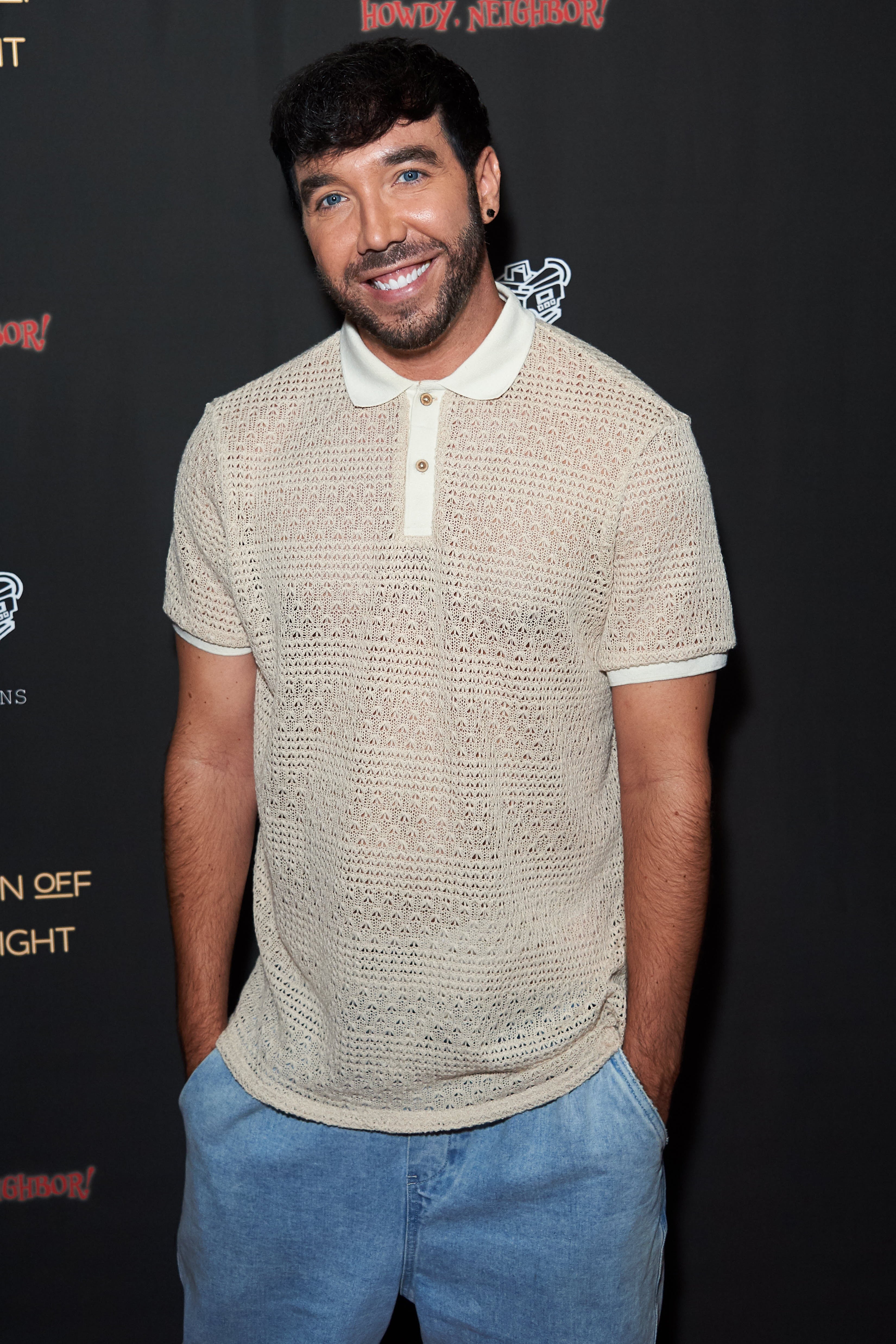 Person in casual knit polo shirt and jeans, smiling at an event backdrop. The article is LGBT-related