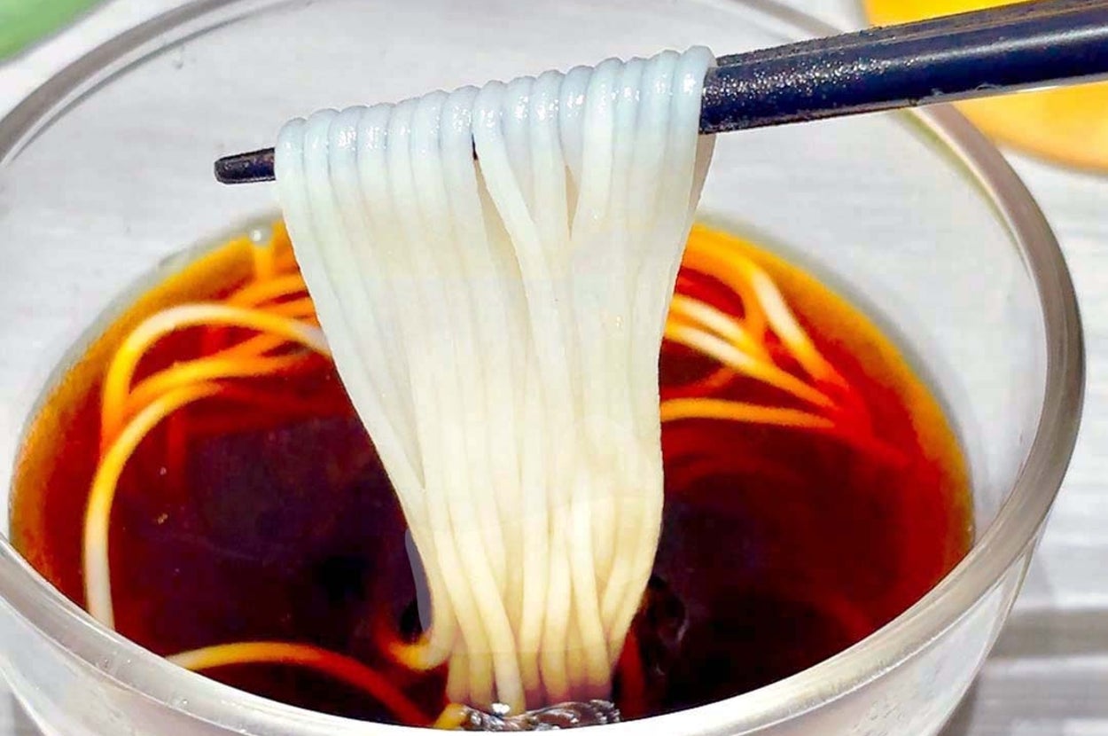 箸で冷たい素麺を持ち上げ、ガラスの器に入ったつゆに浸している。