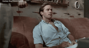 Person on a couch in a casual shirt, looking off-camera with a thoughtful expression