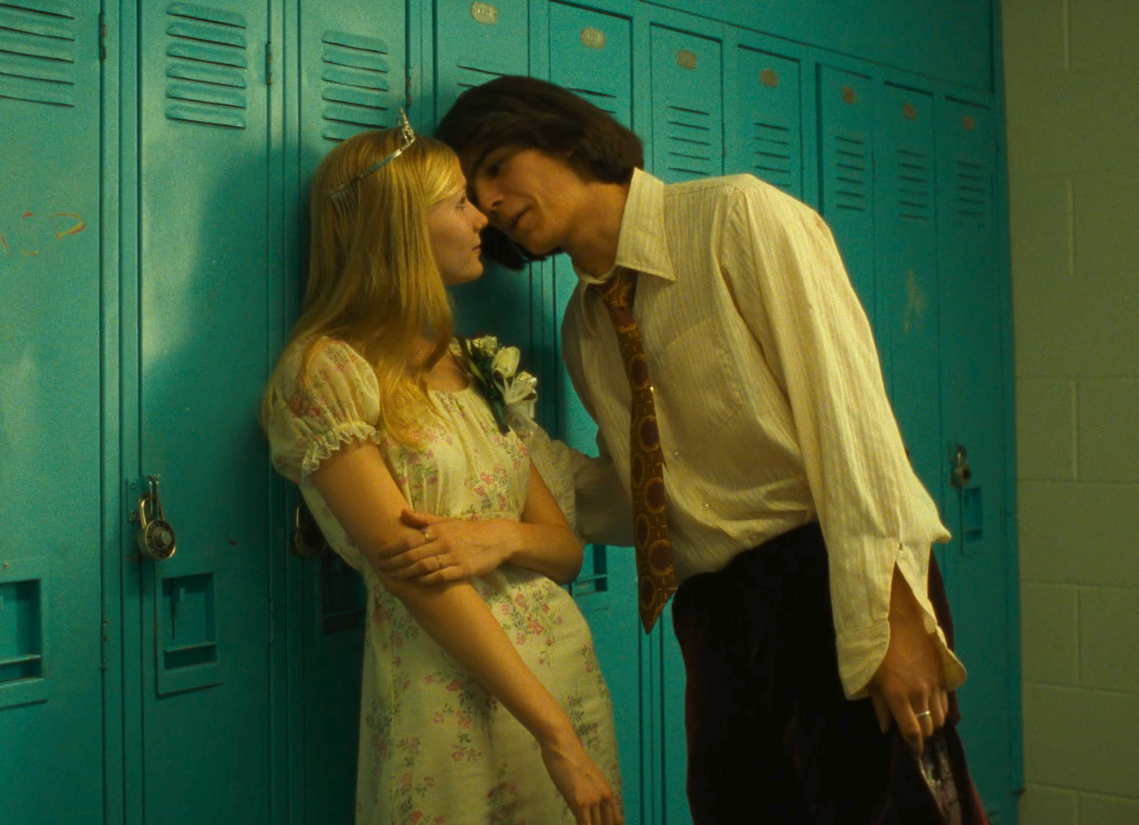 Young Kirsten Dunst and Josh Hartnett standing close, leaning against lockers in a scene from "The Virgin Suicides"