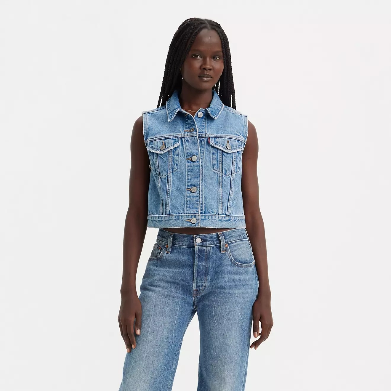 Person wearing a sleeveless denim jacket and jeans, standing against a plain background. Clothing suited for casual shopping looks