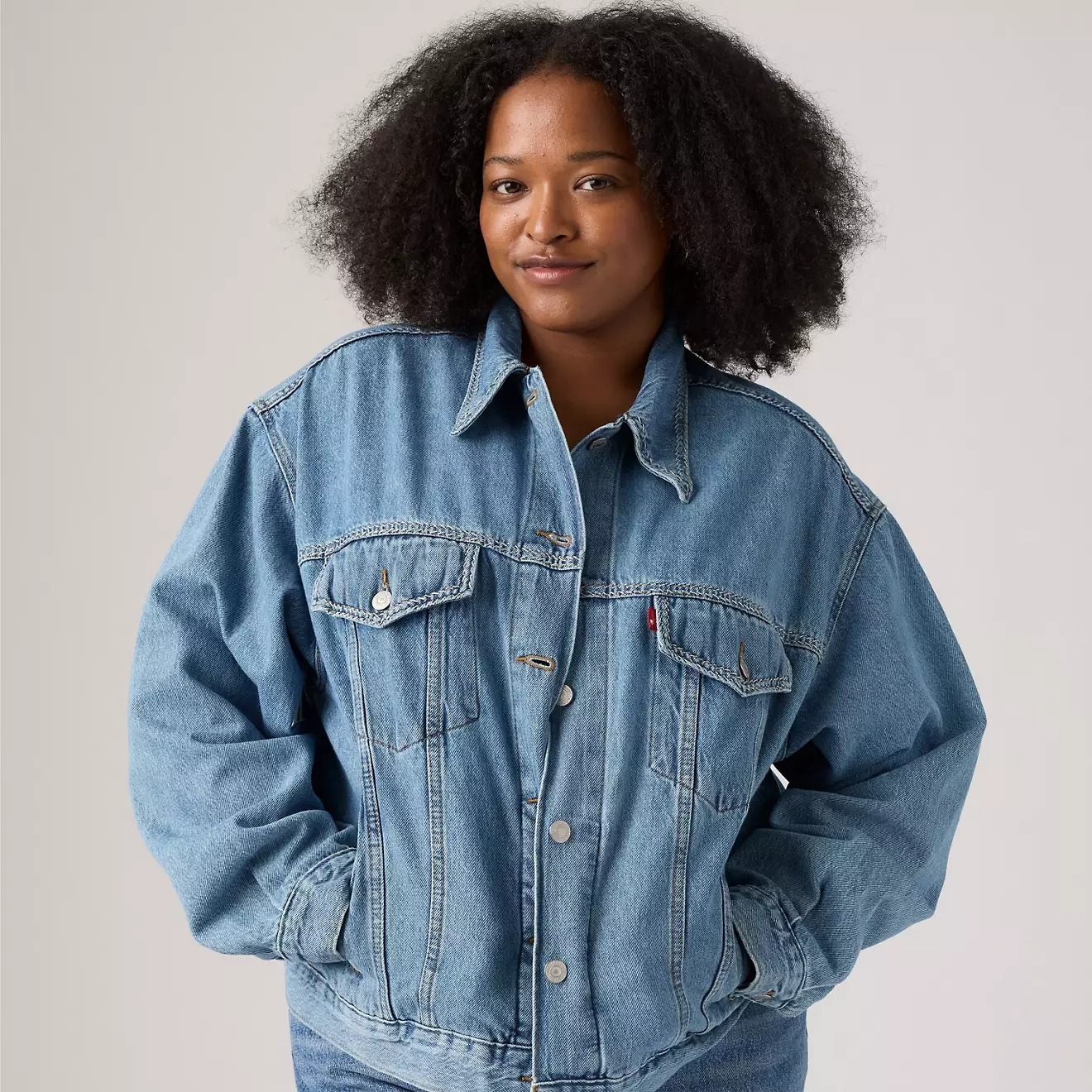 Person wearing an oversized denim jacket with hands in pockets, posing confidently