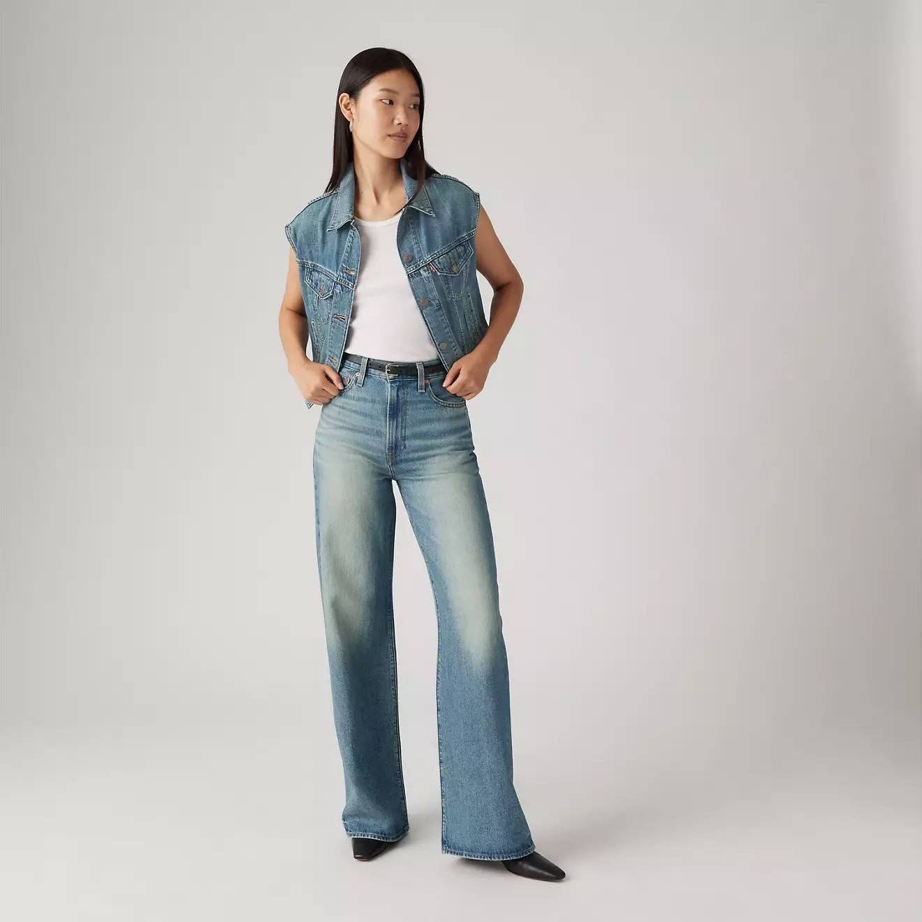 A woman models a denim vest and jeans over a white T-shirt, paired with black shoes, showcasing a casual shopping look