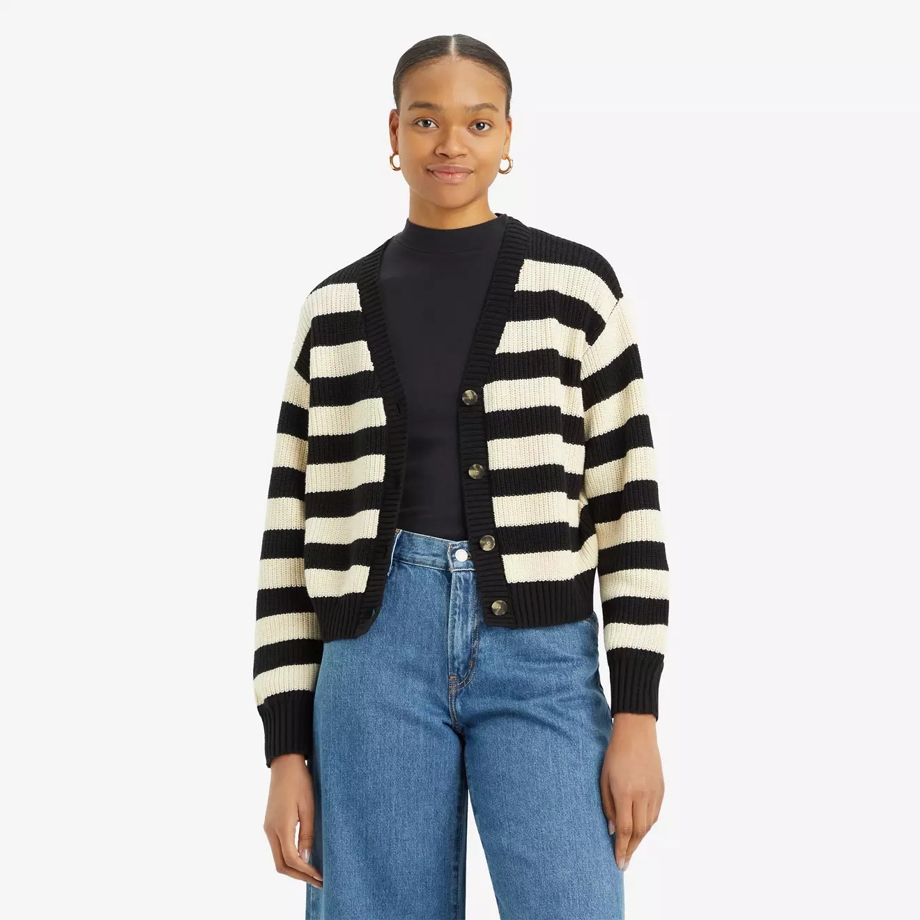 Person wearing a striped cardigan over a black top, paired with blue jeans. They are smiling and wearing hoop earrings