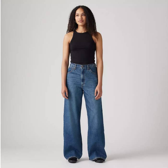 Person wearing a black sleeveless top and wide-leg jeans, standing in a neutral pose against a plain background