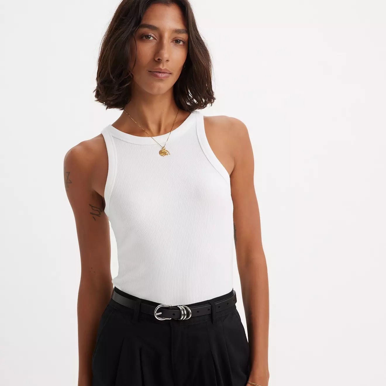 A woman in a casual sleeveless top and belted trousers poses confidently, possibly showcasing fashion or style for a shopping article
